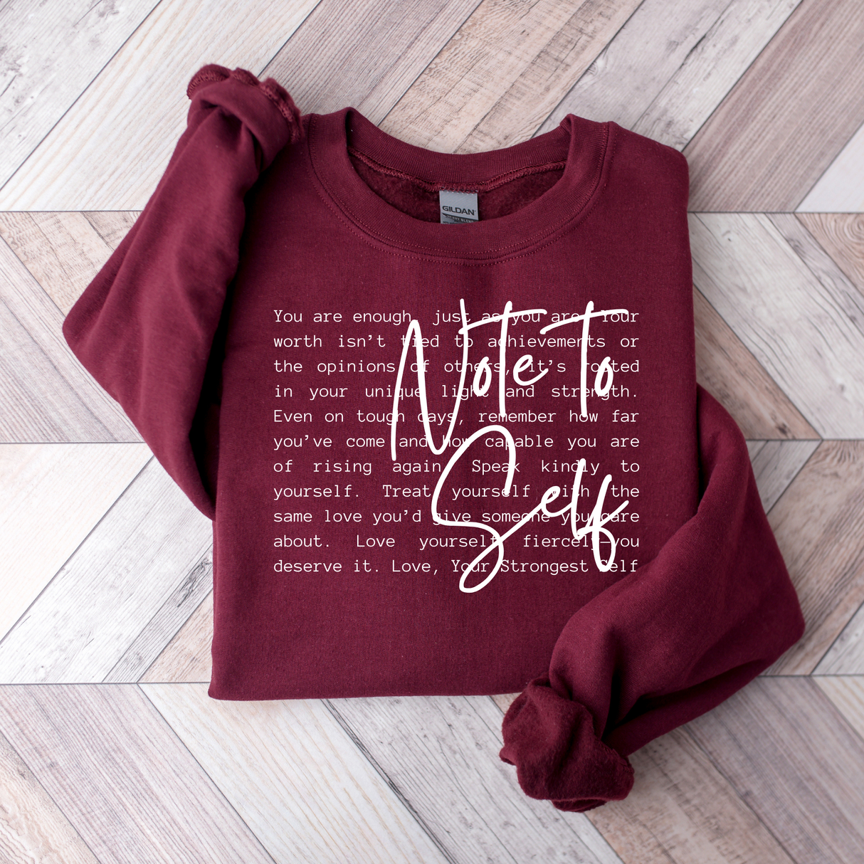 Maroon sweatshirt with motivational text on a wooden floor