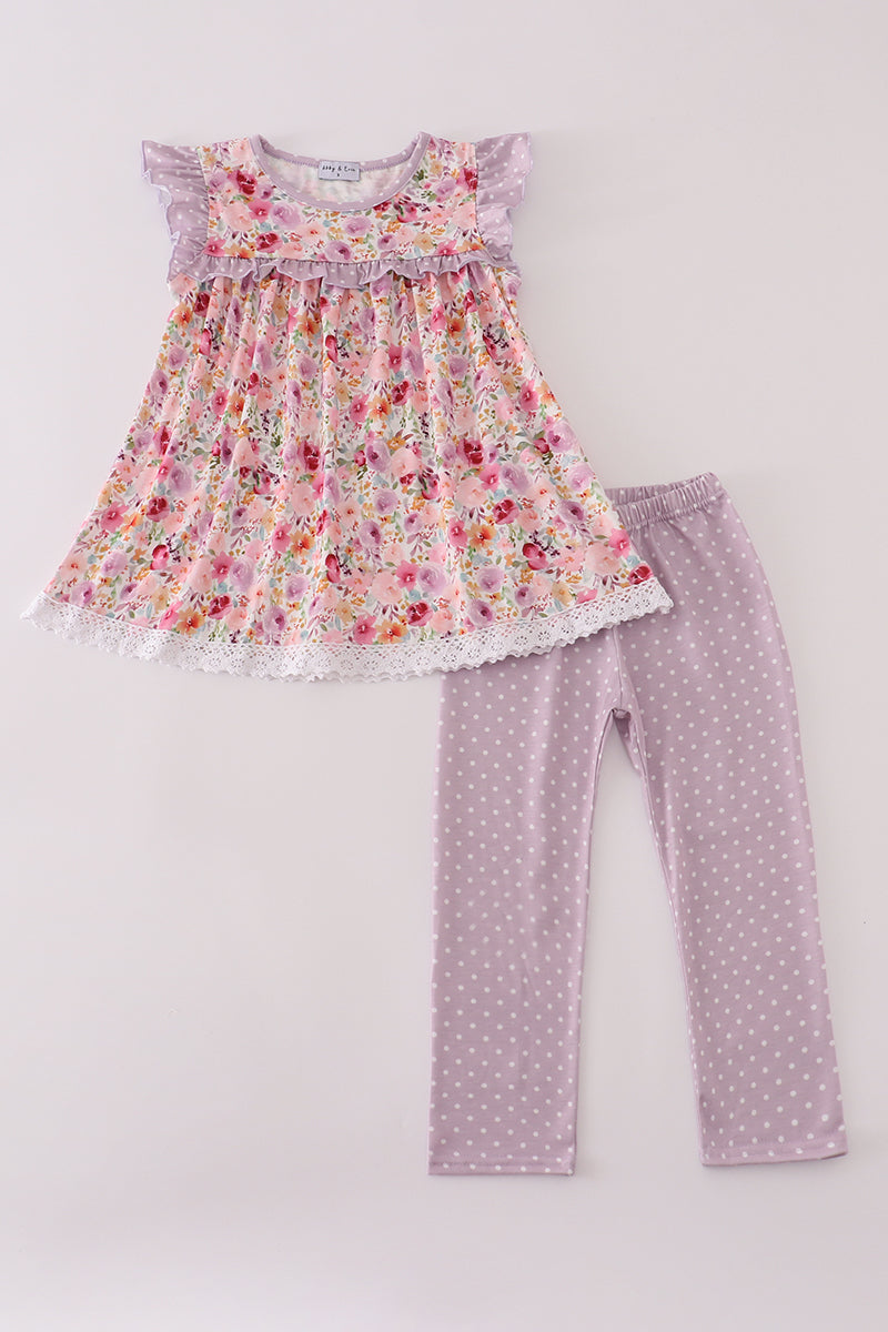 A flat lay of a charming two-piece outfit from the Cottage Bloom collection. The tunic features a soft pink floral print with lavender polka dot flutter sleeves, a ruffled chest, and lace-trimmed hem. Paired with lavender leggings dotted with white polka dots, perfect for everyday play and sister style.
