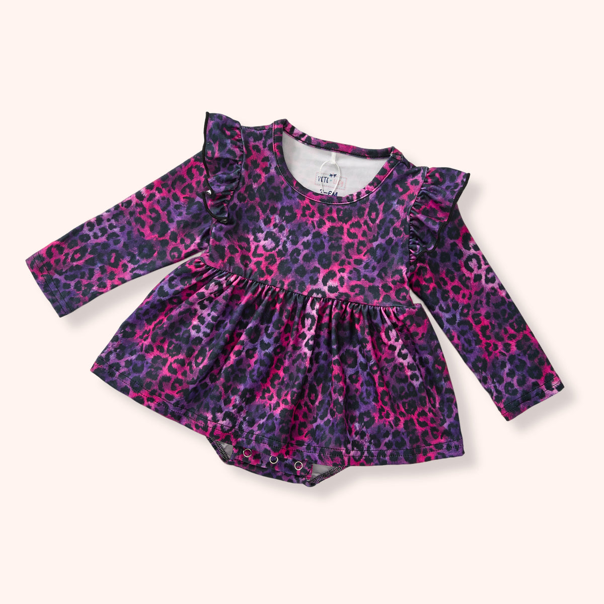 A baby girl's long-sleeve romper dress featuring a purple and pink leopard print pattern, ruffled shoulder details, and a gathered peplum waist, shown on a light cream background.