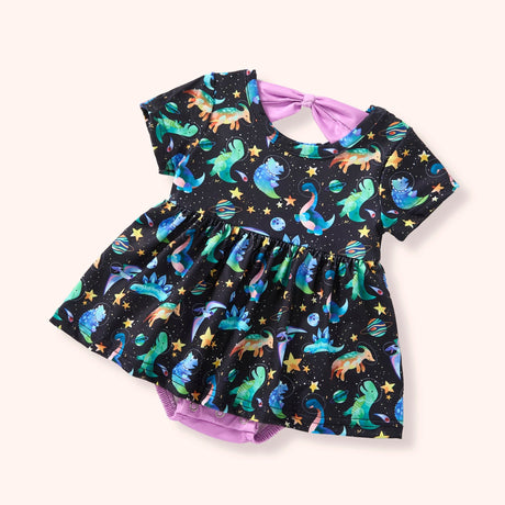Baby skirted romper with colorful space dinosaur print on a black background, featuring short sleeves, a gathered skirt, and snap closures.