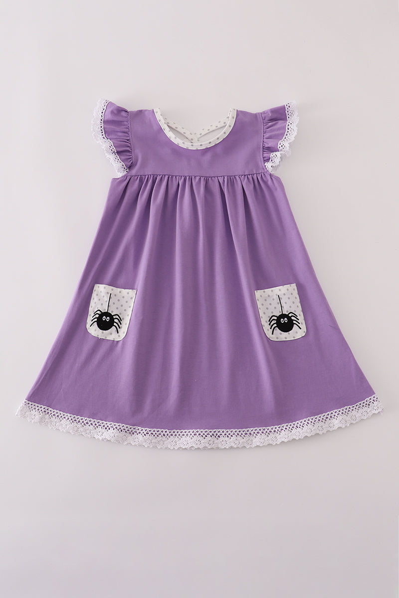 A flat lay of a girls' short-sleeve purple dress featuring white lace trim at the flutter sleeves and hem. The dress has a soft scoop neckline with a polka-dot lining and two front pockets adorned with playful black spider designs on a pale gray background. Made from soft, stretchy milk silk fabric, perfect for Halloween or autumn adventures.