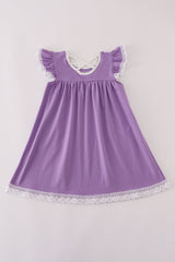 A flat lay of the back side of a girls' purple dress made from soft milk silk fabric. The dress features flutter sleeves trimmed in white lace, a scooped neckline with polka-dot lining, and a charming crisscross strap detail at the upper back. The hem is finished with delicate white lace, adding a sweet touch to this comfortable, twirl-ready Halloween look.