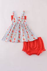 Back view of a baby girl outfit set featuring a sleeveless sundress and matching bloomers. The dress has wide straps and an elastic back waistband, with a blue-and-white striped pattern covered in vertical rows of red apples and greenery. A hint of the red front bow peeks out at the sides. The matching solid red bloomers have soft elastic at the waist and leg openings for a comfy fit.