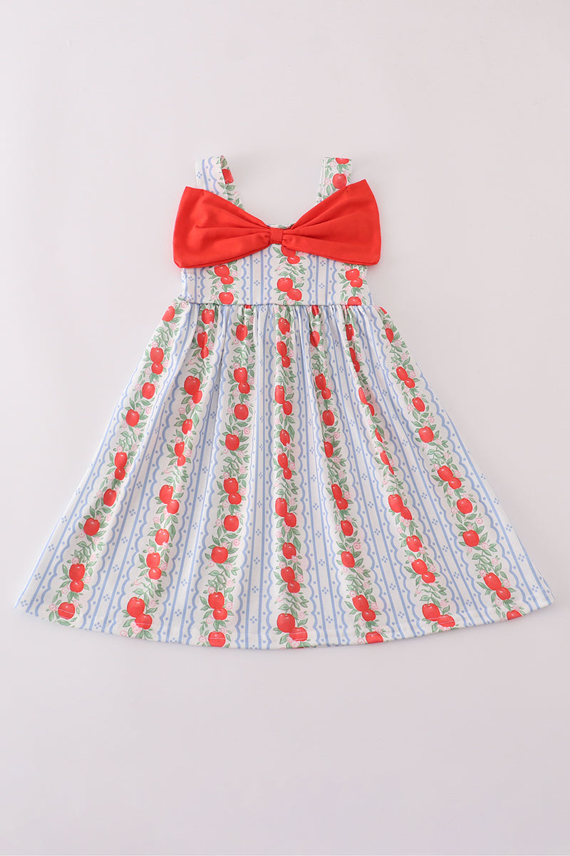 A flat lay of a girls’ sleeveless sundress featuring wide shoulder straps and a flared skirt. The dress has a blue-and-white striped background with vertical rows of red apples and leafy vines. A large red bow decorates the front chest area, adding a playful touch to the classic print. The design is sweet and vintage-inspired, perfect for warm weather.
