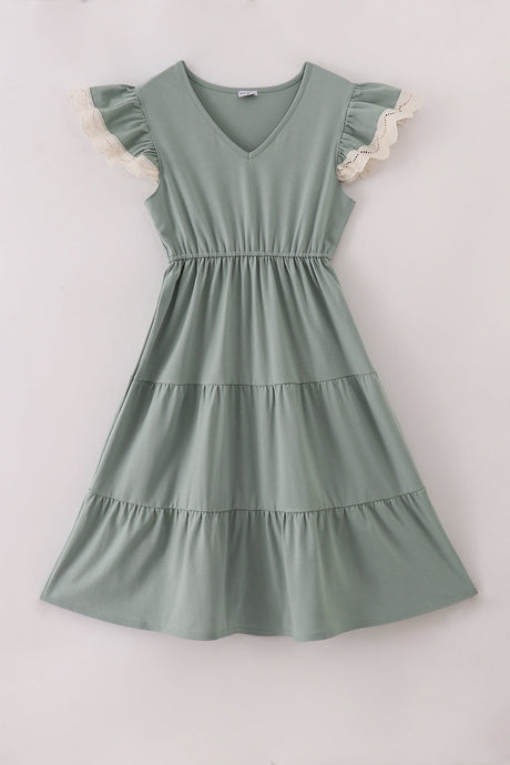 A sage green tiered dress with a V-neckline and ruffled flutter sleeves trimmed in delicate ivory lace, laid flat on a light background. The dress features an elastic waistband and three gathered tiers for a soft, flowy silhouette.