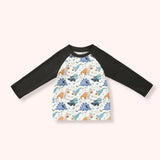 Boys cream Halloween dinosaur raglan shirt with black long sleeves, pumpkins, bats and blue and teal dinosaurs.