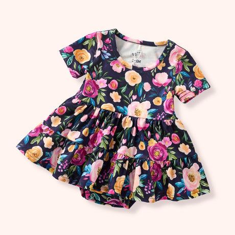 Flat lay of a dark skirted romper with straight short sleeves, bold floral patterning, and snap closure.