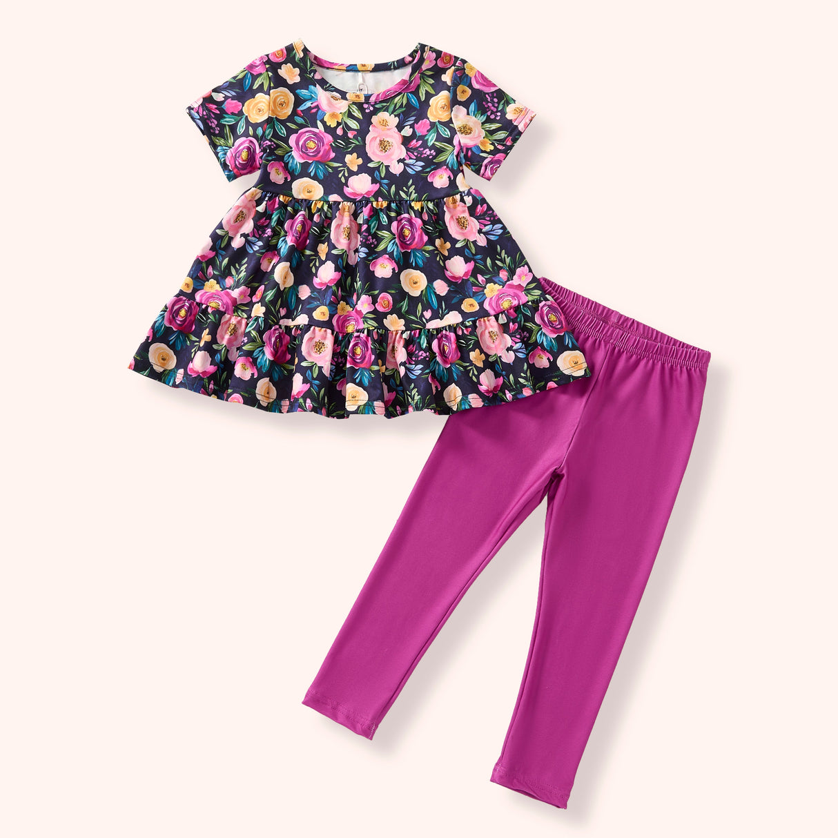 Flat lay of a girls outfit set featuring a dark floral short-sleeve tiered tunic paired with pink leggings.