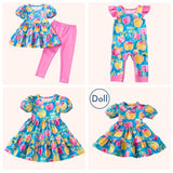 A flat lay collage showcasing the Pete + Lucy A+ Apples Collection: a peplum top and leggings set, a baby ruffle romper, a tiered dress, and a coordinating doll dress. Each piece features the same vibrant apple print on a turquoise blue background.