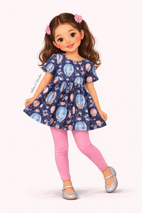 Illustrated girl wearing a navy short-sleeve tunic featuring pastel hot air balloons with floral accents paired with soft pink leggings.