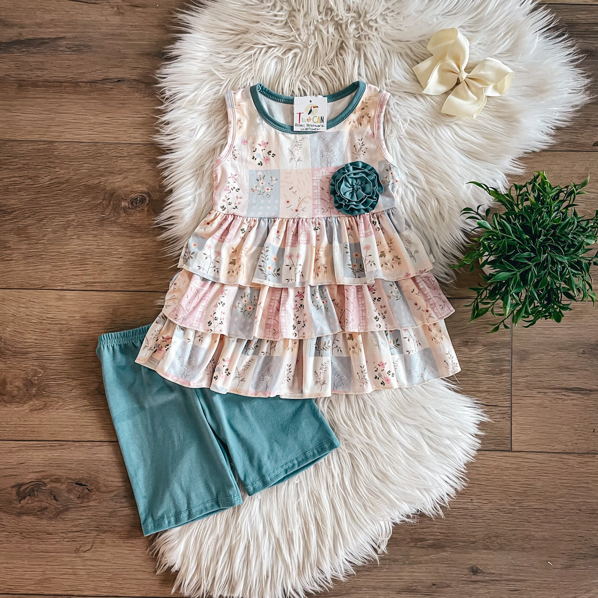 Girls’ patchwork peplum top with teal flower and teal bike shorts, laid flat on faux fur rug.