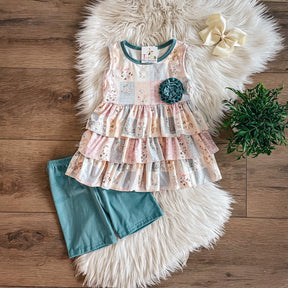 Girls’ patchwork peplum top with teal flower and teal bike shorts, laid flat on faux fur rug.