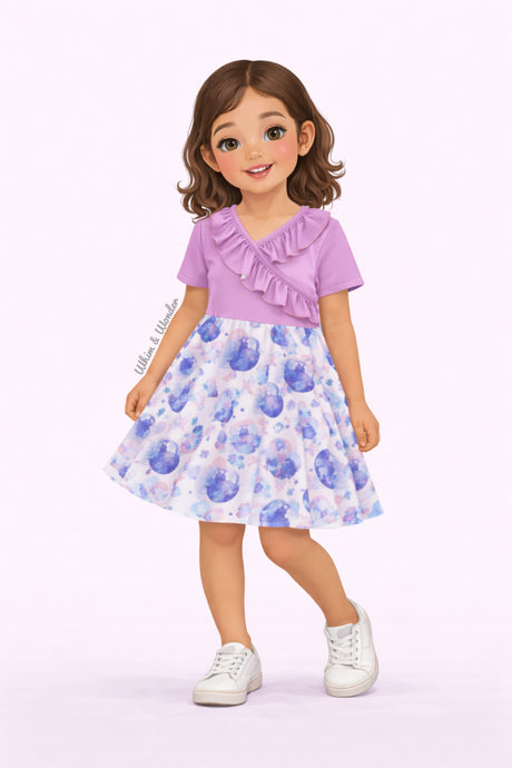 Illustrated girl wearing a lavender short-sleeve dress with ruffle neckline and pastel celestial print featuring moons, stars, clouds, and rainbows