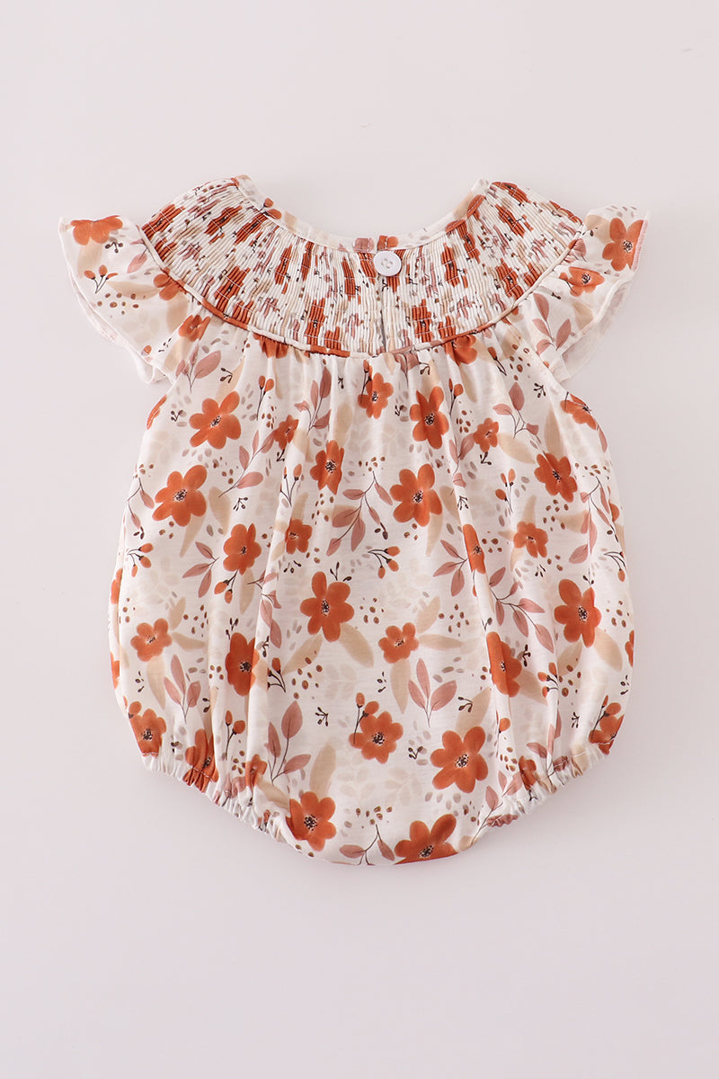 Back view of a cream-colored baby romper featuring rust-orange floral print and a wide smocked neckline with flutter sleeves. A single button closure is centered at the top of the back, and elastic leg openings provide a snug, comfy fit.