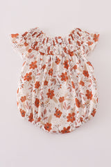 Back view of a cream-colored baby romper featuring rust-orange floral print and a wide smocked neckline with flutter sleeves. A single button closure is centered at the top of the back, and elastic leg openings provide a snug, comfy fit.