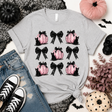 A heather gray short-sleeve tee featuring a grid of pink pumpkins, black bows and black cats printed on the front. 
