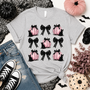A heather gray short-sleeve tee featuring a grid of pink pumpkins, black bows and black cats printed on the front. 