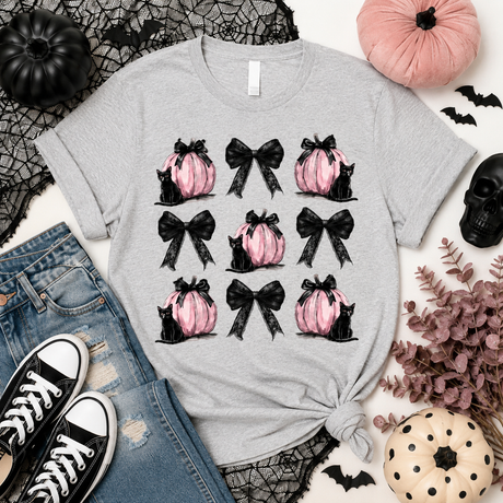A heather gray short-sleeve tee featuring a grid of pink pumpkins, black bows and black cats printed on the front. 