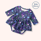 Flat lay of the Breezy Blossoms purple floral baby bubble romper with three-quarter sleeves, a gathered skirt, and diaper snaps.