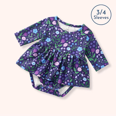 Flat lay of the Breezy Blossoms purple floral baby bubble romper with three-quarter sleeves, a gathered skirt, and diaper snaps.