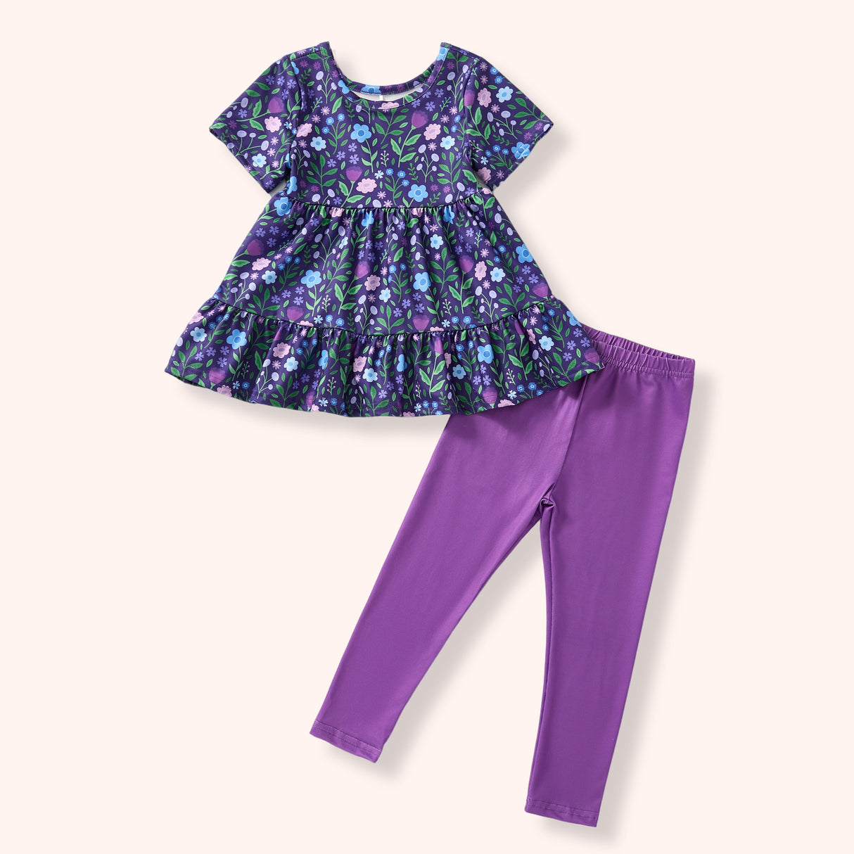 Flat lay of a purple floral short-sleeve tunic with a gathered waist, ruffled hem, and coordinating solid purple leggings.