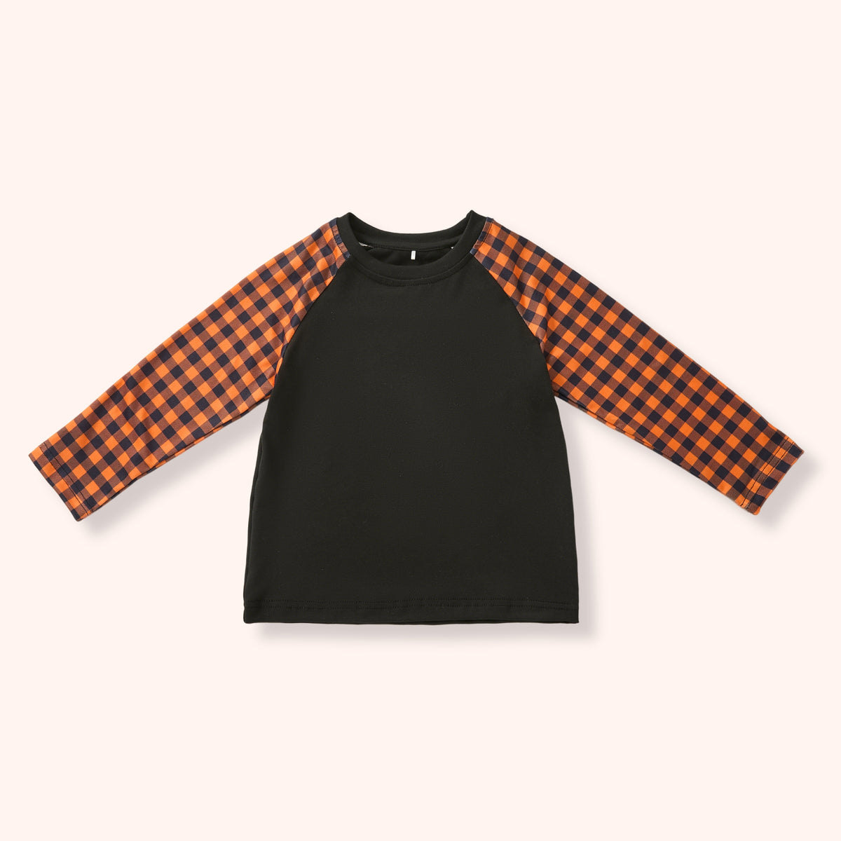 A children's long-sleeve raglan shirt with a solid black body and orange-and-black buffalo plaid sleeves, laid flat on a light cream background.