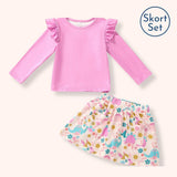 A children's two-piece outfit set featuring a pink long-sleeve top with ruffled shoulders and a matching printed skirt with colorful dinosaurs and flowers, shown on a light cream background with a 'Skort Set' label in the top right.