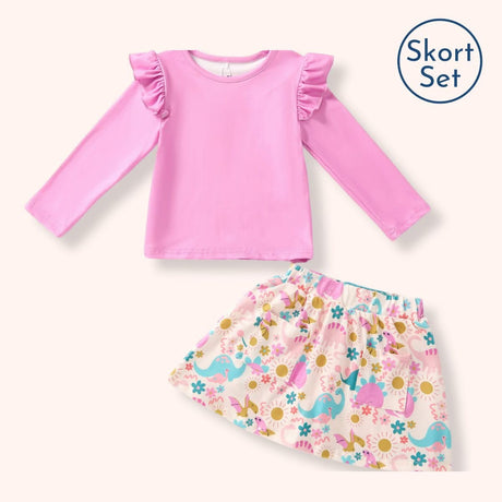 A children's two-piece outfit set featuring a pink long-sleeve top with ruffled shoulders and a matching printed skirt with colorful dinosaurs and flowers, shown on a light cream background with a 'Skort Set' label in the top right.