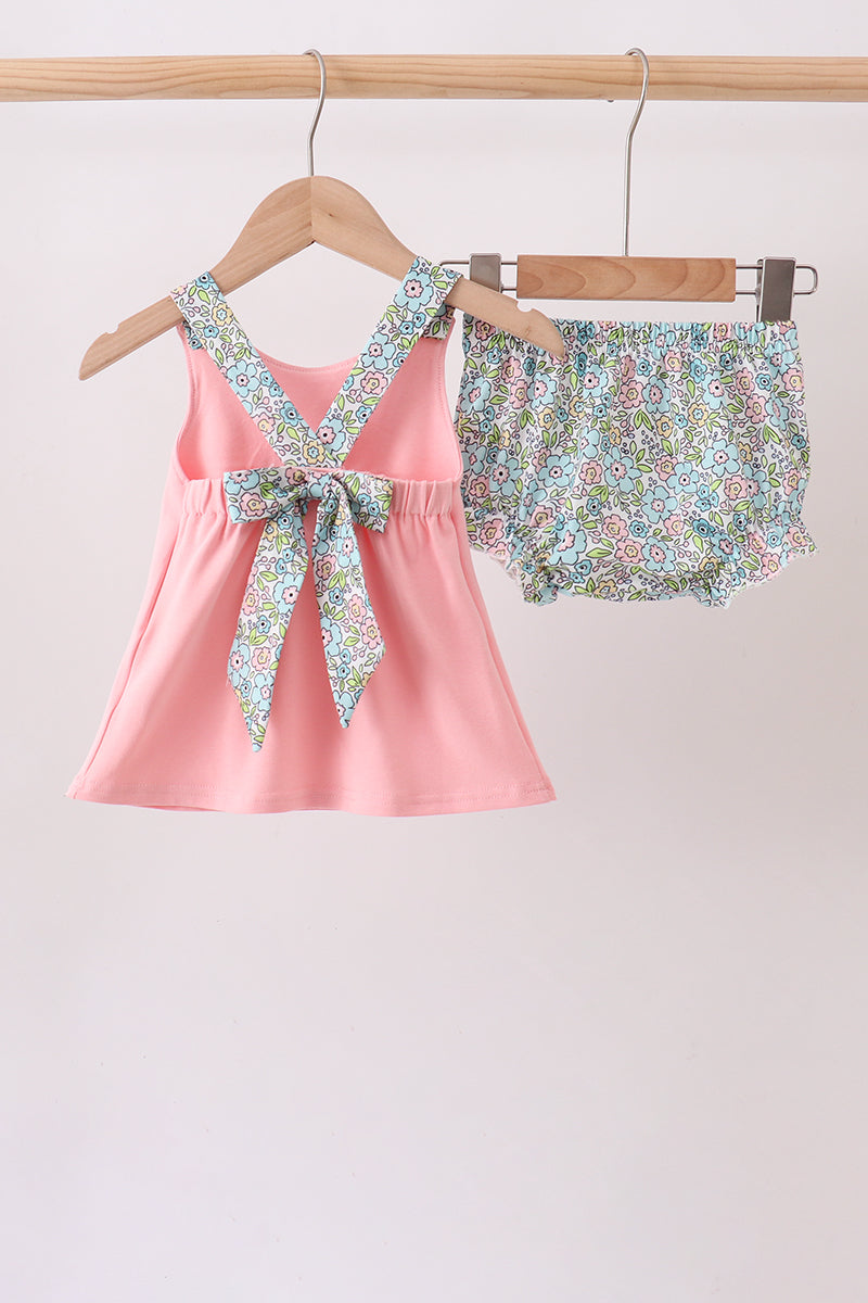 Back of pink chick tunic showing crossed floral straps and a large tie bow, paired with matching floral ruffle bloomers.