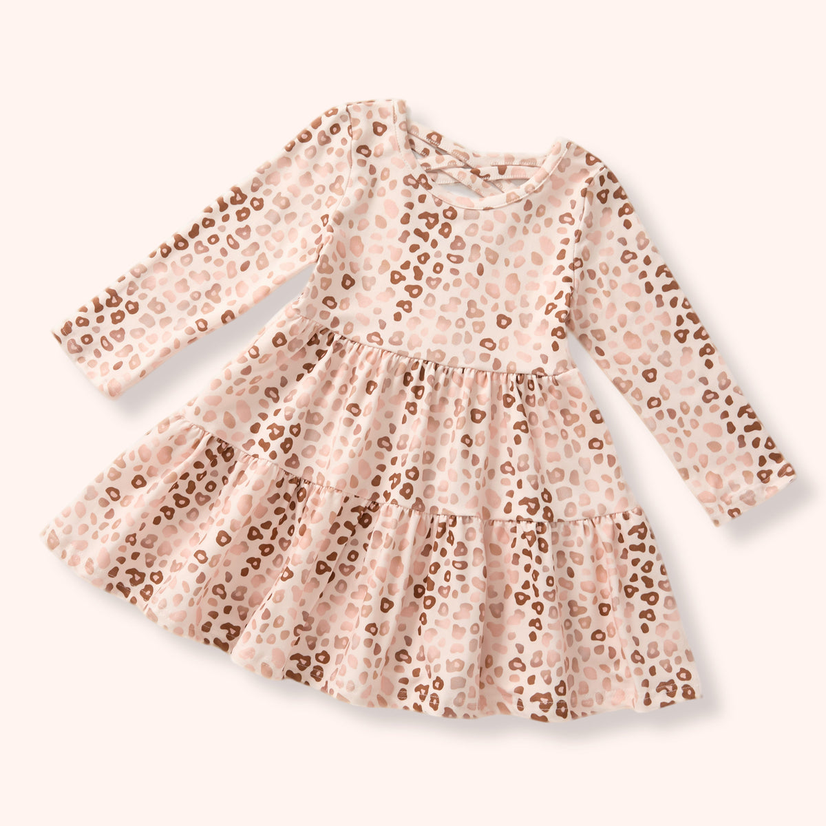 A long-sleeve baby dress with a tiered skirt, featuring a light pink and beige leopard print pattern with brown spots, shown on a solid pale pink background.