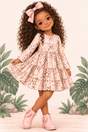 An illustrated girl with long curly brown hair wearing a pink tiered dress with a brown leopard print, a pink bow in her hair, and pink boots, posed against a tropical leaf backdrop.