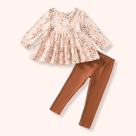 A girl's two-piece outfit set featuring a long-sleeve peplum top in a light pink and beige leopard print, paired with solid rust-brown leggings, laid flat on a light cream background.