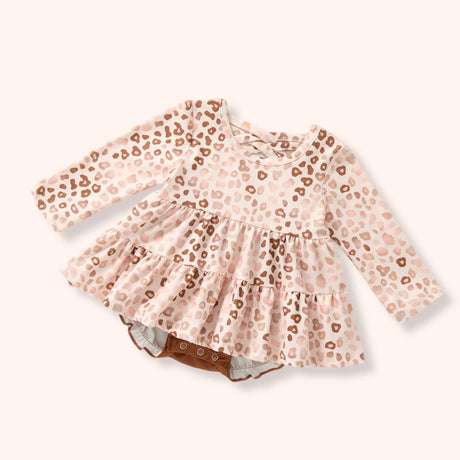 A baby girl's long-sleeve romper dress in a light pink and beige leopard print, featuring a ruffled peplum waist and snap closures at the crotch, shown on a solid pale pink background.