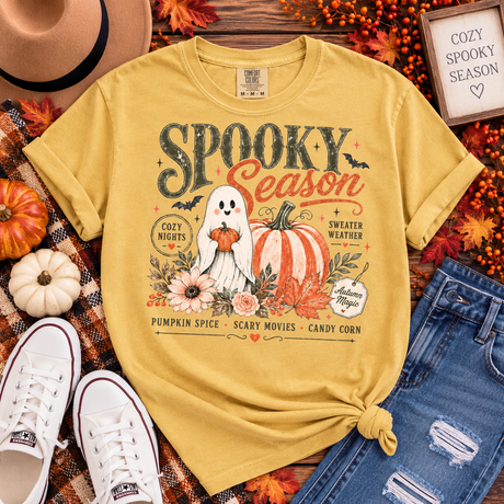 Mustard yellow Comfort Colors tee with a retro “Spooky Season” graphic featuring a smiling ghost, pumpkins, florals, bats and cozy fall sayings.