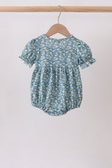Back view of the baby bubble in a blue floral print with puff sleeves, gathered waist, and elastic leg openings.