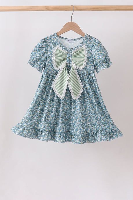 Girls’ blue floral dress with puff sleeves, a ruffled hem, and an oversized sage-striped bow trimmed in white lace.