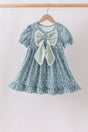 Girls’ blue floral dress with puff sleeves, a ruffled hem, and an oversized sage-striped bow trimmed in white lace.