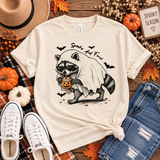 Natural cream tee featuring a raccoon in sunglasses and a ghost costume holding a jack-o’-lantern drink, with bats and “Spooky and Feral” text.
