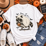 White tee featuring a raccoon in sunglasses and a ghost costume holding a jack-o’-lantern drink, with bats and “Spooky and Feral” text.