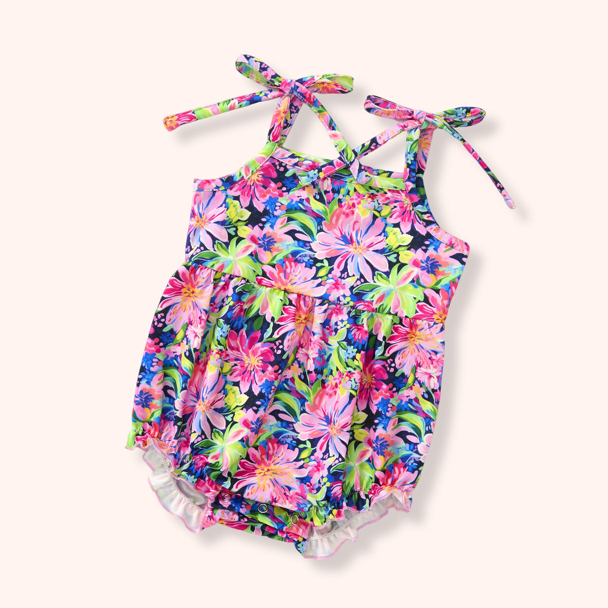 Bright floral baby bubble romper with navy background, pink and purple blooms, tie shoulders, gathered waist and ruffle leg trim.