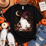 Black tee featuring a whimsical ghost in a plum witch hat holding a glowing lantern, surrounded by a crescent moon, florals, stars and fall foliage.