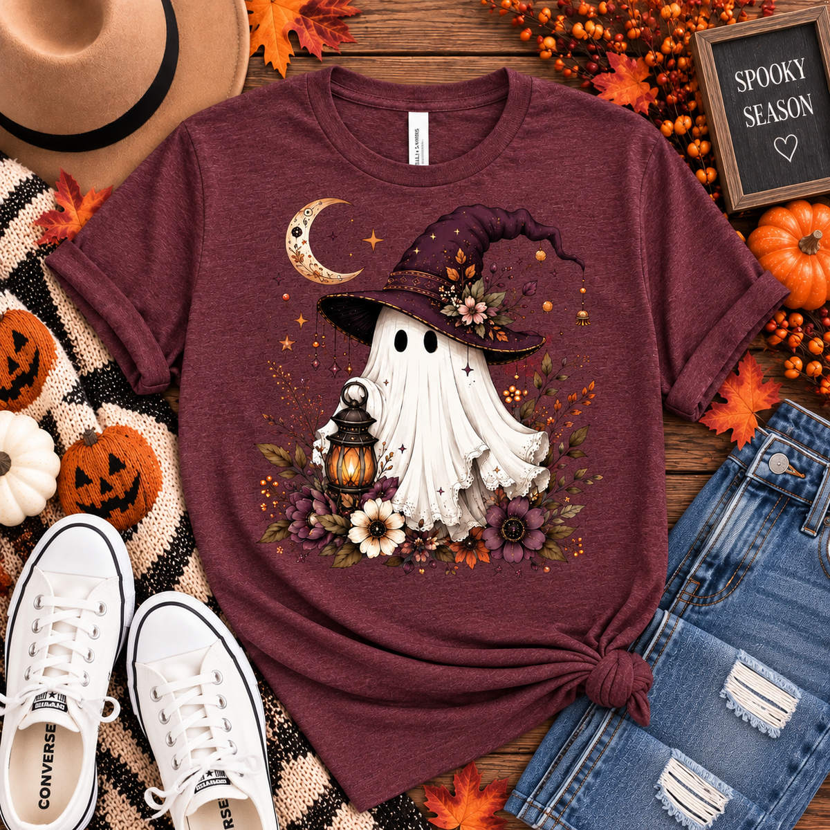 Heather maroon tee featuring a whimsical ghost in a plum witch hat holding a glowing lantern, surrounded by a crescent moon, florals, stars and fall foliage.