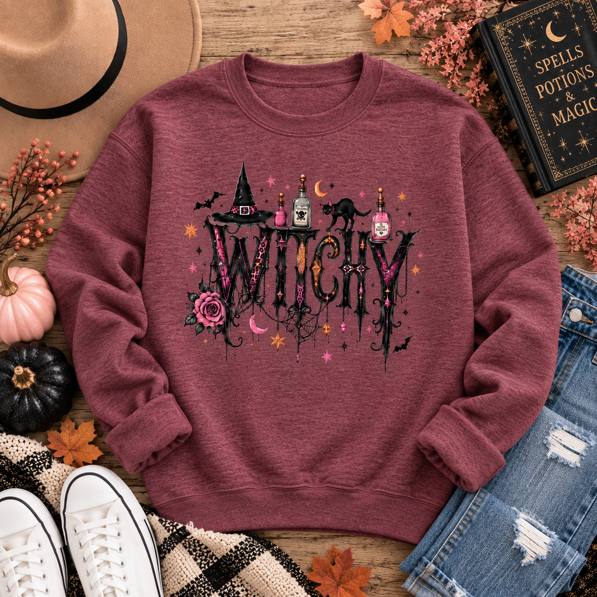 Heather maroon crewneck sweatshirt with a gothic “WITCHY” graphic featuring potion bottles, a black cat, witch hat, rose, bats, moon and stars.