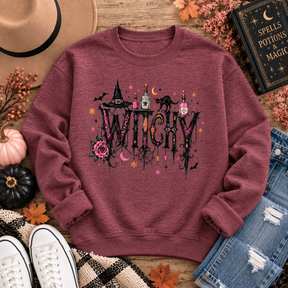 Heather maroon crewneck sweatshirt with a gothic “WITCHY” graphic featuring potion bottles, a black cat, witch hat, rose, bats, moon and stars.