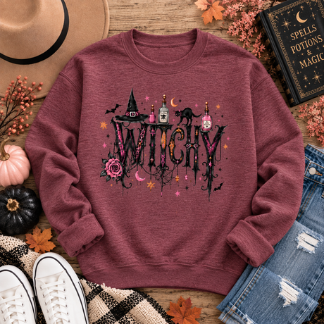 Heather maroon crewneck sweatshirt with a gothic “WITCHY” graphic featuring potion bottles, a black cat, witch hat, rose, bats, moon and stars.